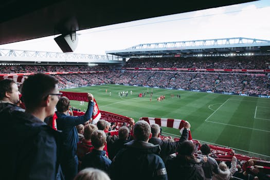 Fans cheer as players take the field at a vibrant football stadium, creating an electric atmosphere.